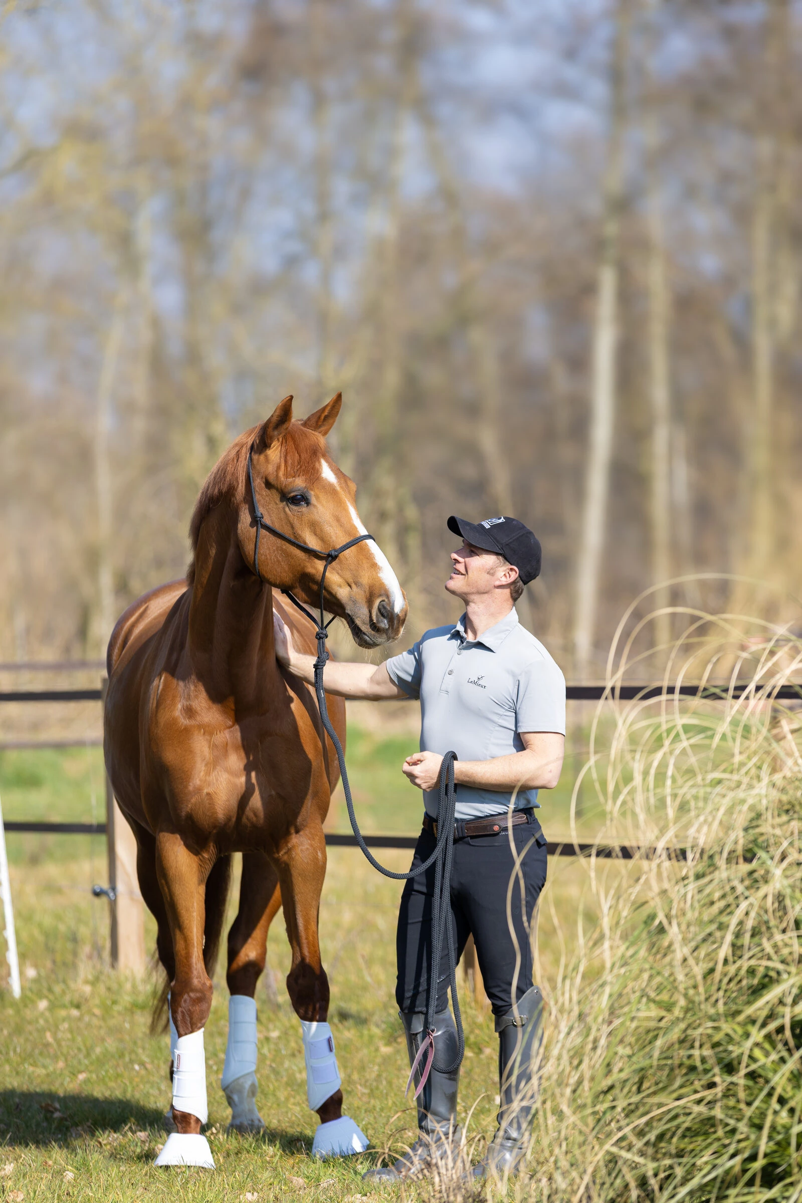 Tristan Tucker standing with a chestnut horse in the field, resting a hand on his neck