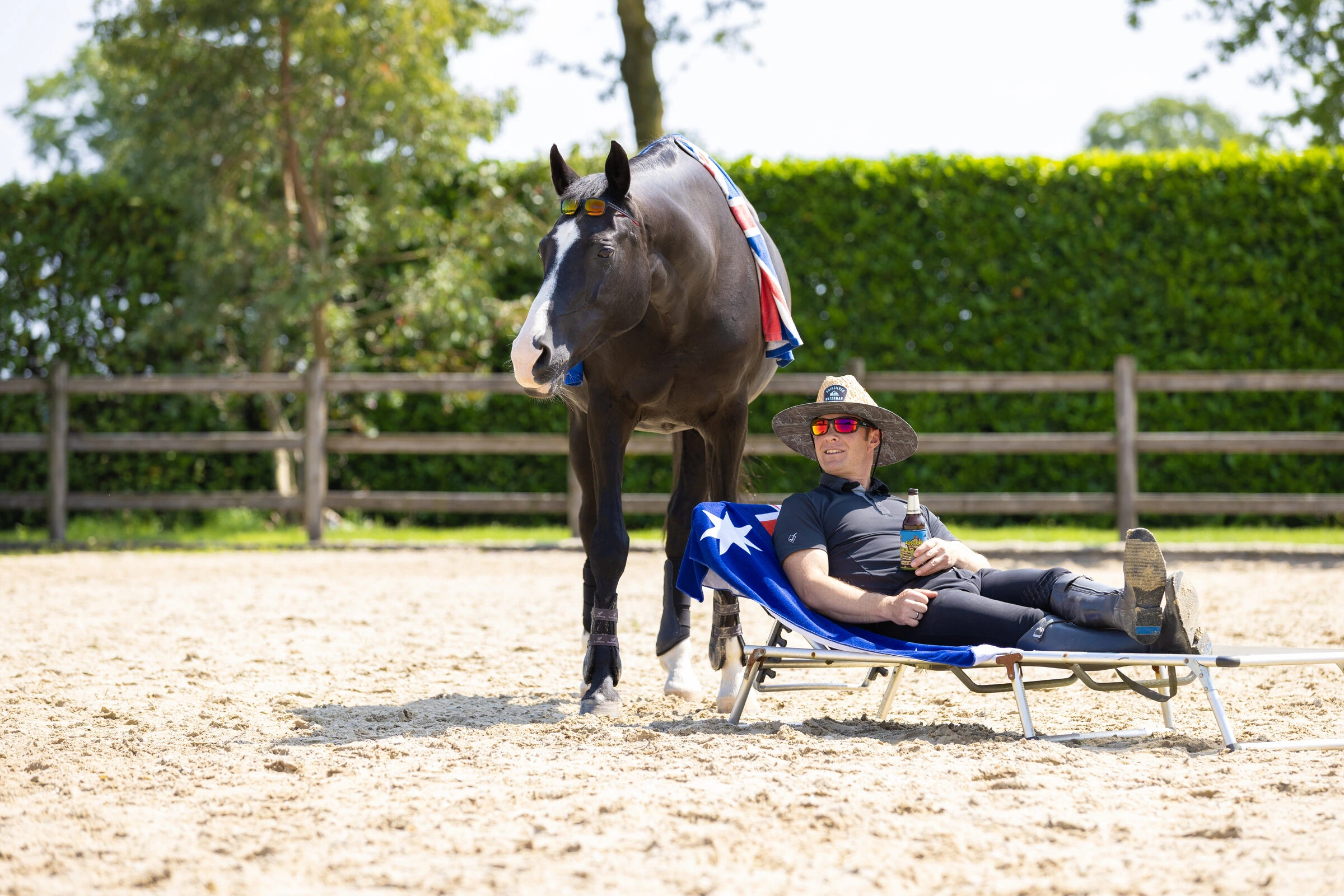 A relaxed horse standing beside a rider resting in an arena