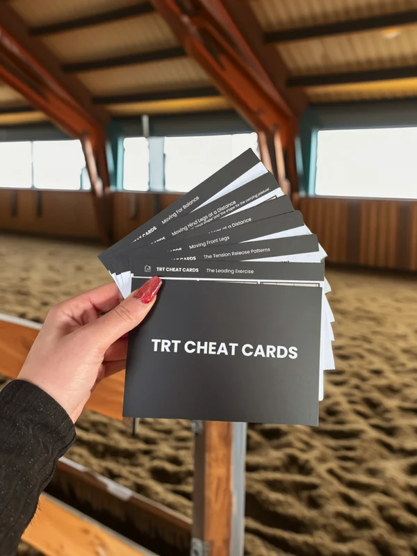 A hand holding the fanned-out TRT Cheat Cards in an indoor riding arena