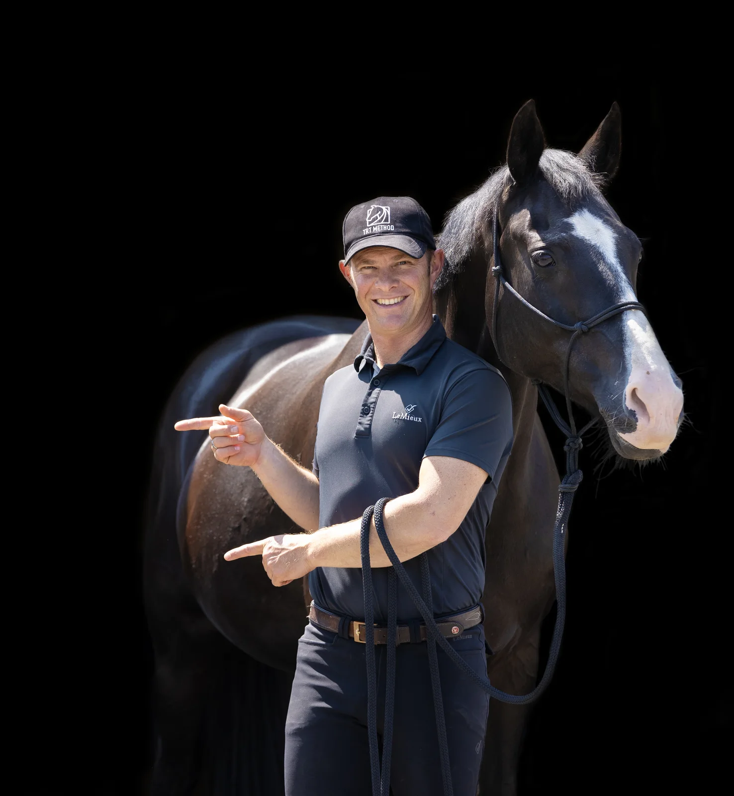 Tristan Tucker smiling and pointing beside a black horse