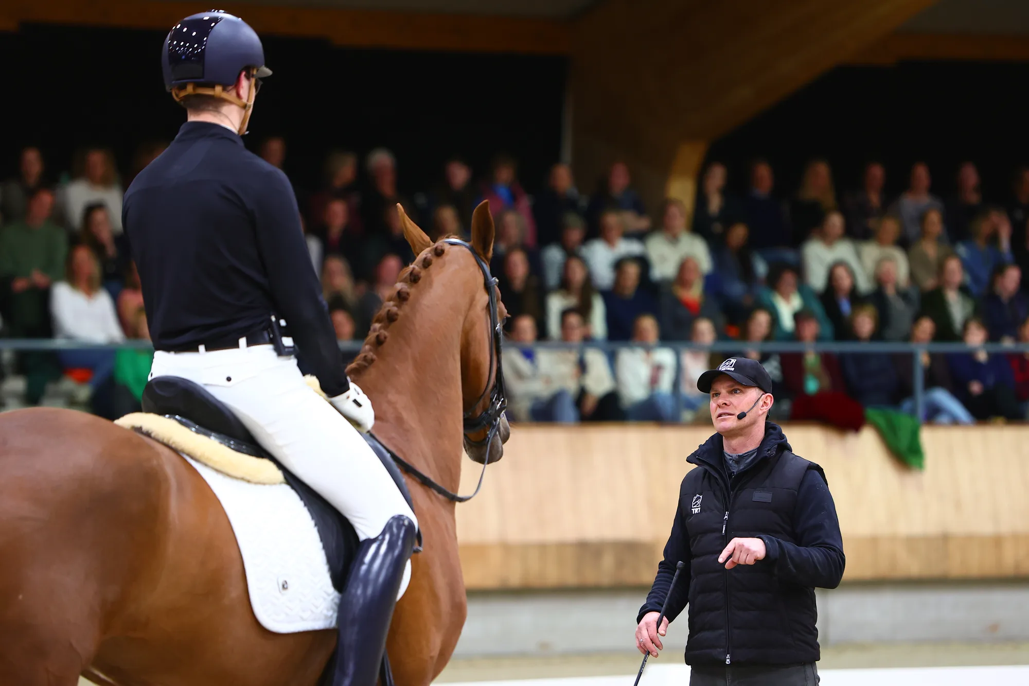Tristan Tucker coaching a rider and horse in front of a full audience