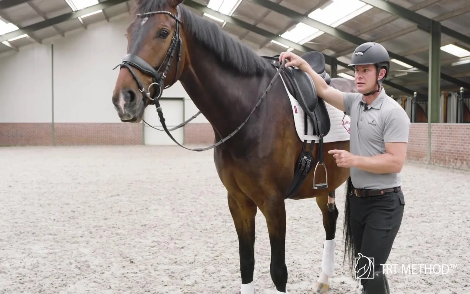 Tristan Tucker simulating the rider's rein aids from the ground beside a saddled horse
