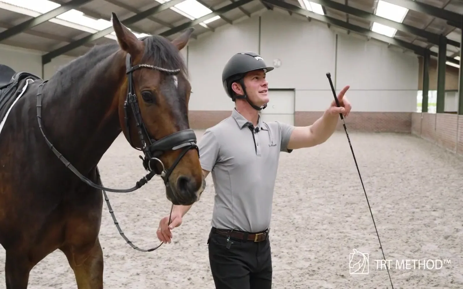 Tristan Tucker explaining the hot horse beside a saddled bay horse in an indoor arena