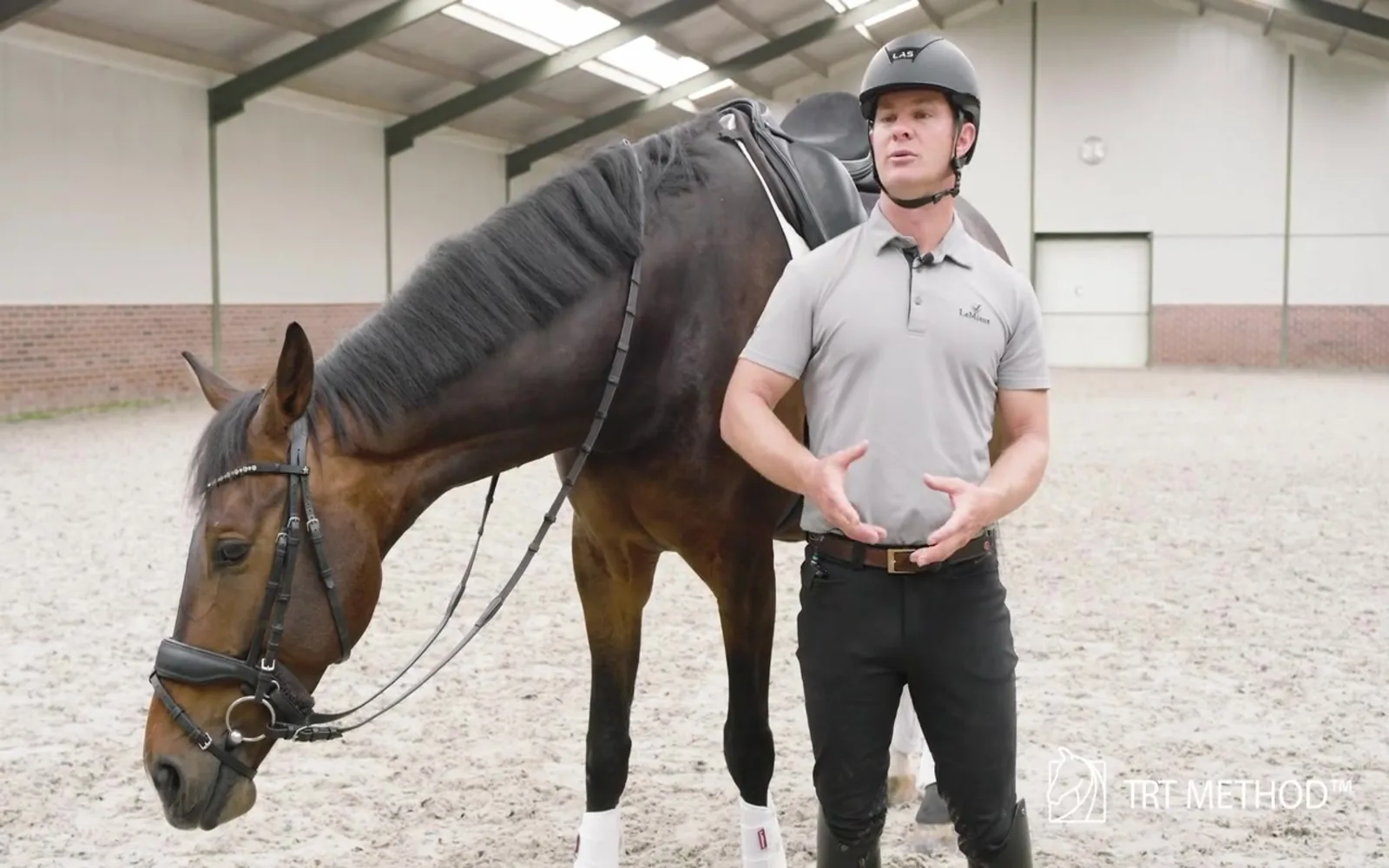 Tristan Tucker talking through a pattern while a bay horse stands relaxed beside him